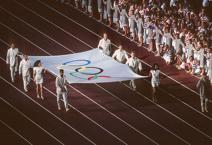 Sis esportistes i dos voluntaris entrant la bandera olímpica a l’Estadi durant la inauguració.