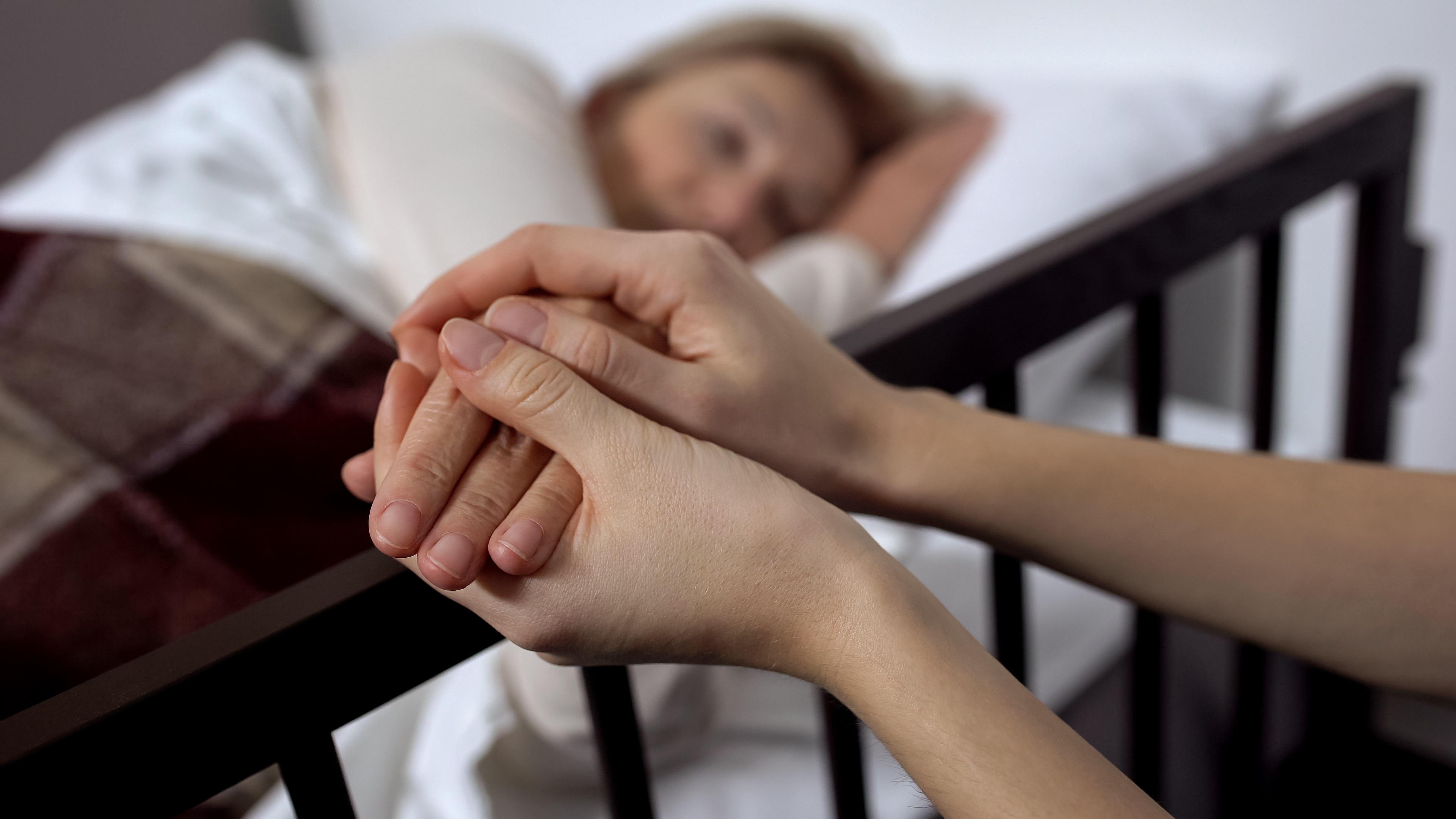 Una filla agafant la mà de la seva mare malalta terminal